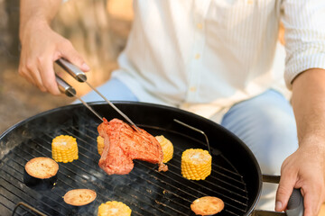 Young man cooking meat on grill at barbecue party, closeup