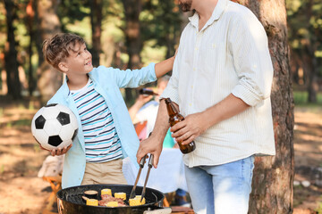 Little boy with ball and his father cooking food on grill at barbecue party