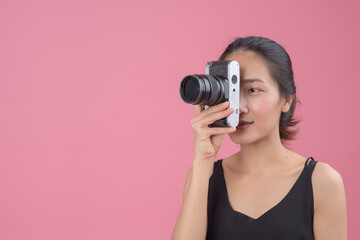 .Portrait of a young asian woman  holding photo camera and looking away at copy space isolated over pink background. Female photography in action.