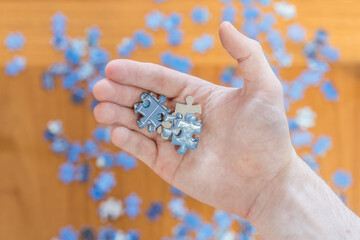 Hand holding blue jigsaw puzzle pieces. Difficult challenge concept. Person trying to build a puzzle on table top view close up