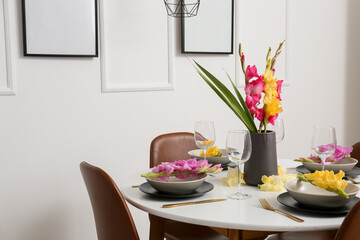 Dining table with stylish setting and beautiful Gladiolus flowers in light room