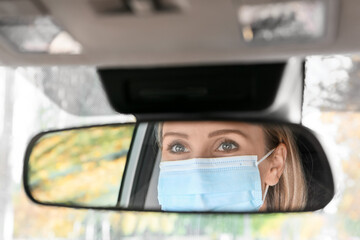 Reflection of female driver wearing medical mask in car rear view mirror