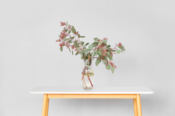 Vase with plant branches on wooden table near grey wall