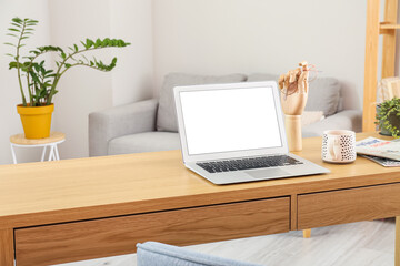 Workplace with modern laptop, cup and magazines in room