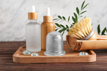 Board with bottles of cosmetic products and vacuum jar for anti-cellulite massage and brush on wooden table