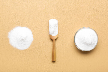 Bowl, spoon and pile of baking soda on beige background