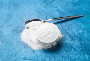 Bowl with baking soda and spoon on blue background