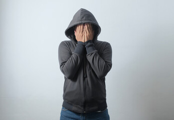 portrait of hooded man covering his face using hands