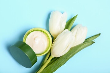 Bouquet of beautiful white tulips and jar of facial cream on blue background