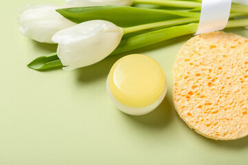 Jar of cream with makeup sponges and tulips on green background. Mother's Day celebration