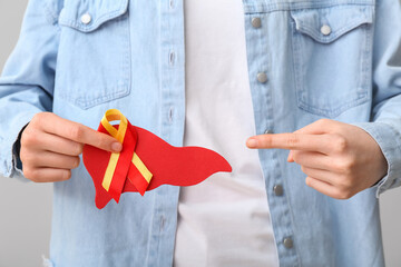 Woman pointing at awareness ribbon and paper liver on grey background, closeup. Hepatitis concept