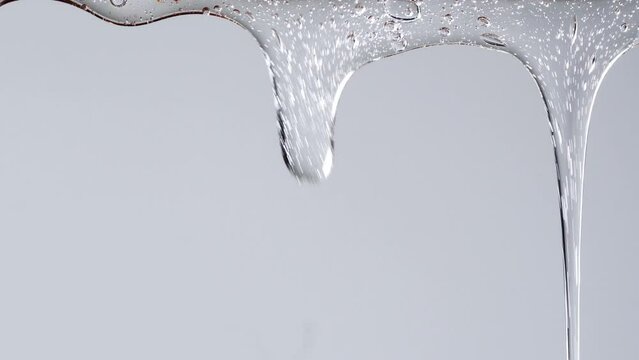 Closeup shot of transparent cosmetic gel fluid flowing on white background.
