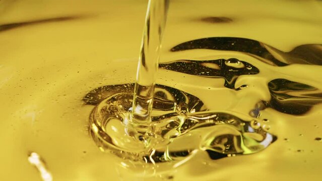 Closeup shot of pouring golden olive oil in slow motion, healthy food background
