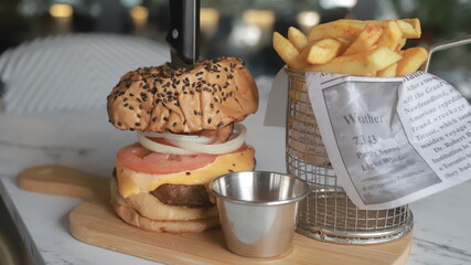 hamburguesa alta con patatas fritas en una pequeña cesta de freír y un bol de ketchup en la...