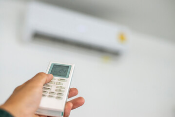 Fototapeta premium An air conditioner in a room with a young person using a remote control is turning on the air conditioner during the sweltering day at home.