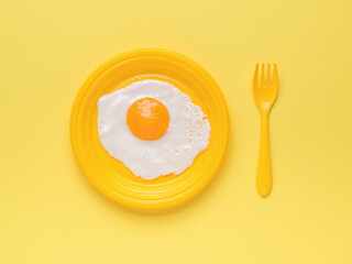 A yellow bowl with a fried egg and a yellow fork on a yellow background. Minimal concept. A popular breakfast.