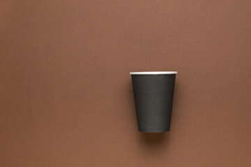 Black paper cup on a brown background. Minimal concept.