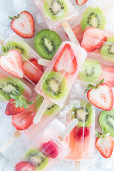Top down view of a pile of refreshing strawberry kiwi popsicles on ice.