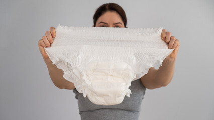 A caucasian woman holds an adult diaper and checks its strength on a white background.  - obrazy, fototapety, plakaty