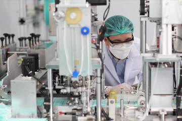 Naklejka premium Worker in personal protective equipment or PPE inspecting quality of mask and medical face mask production line in factory, manufacturing industry and factory concept.