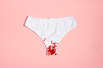White women's panties with red flower sequins on a pastel pink background. - obrazy, fototapety, plakaty
