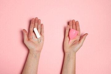 Female hands holding pink silicone menstrual cup and cotton tampon for critical days. Choice of feminine hygiene products. Zero waste and healthy lifestyle concept.