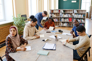 High angle view shot of mature teacher working with multi-ethnic group of immigrant students in library - obrazy, fototapety, plakaty