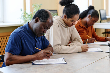 Group of three Black people learning English at school for immigrants sitting at table doing...