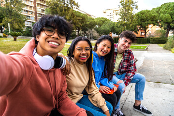 Group of multiracial college student friends taking selfie with phone outside. Students laughing...
