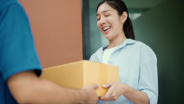 Beautiful Young Woman receiving parcel from blue uniform delivery man f the house with good service from shopping online. Courier man delivering a cardboard box postal package to destination.