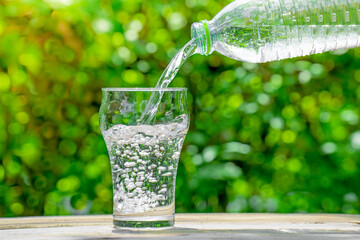 Pour water from a plastic bottle into a glass. The background of the plants in the garden.