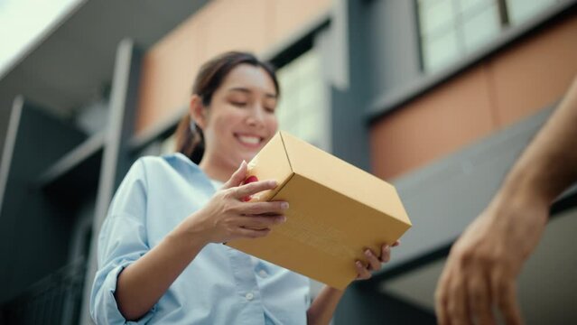 Close up parcel in hand of blue uniform delivery man to customer front of the house with good service from shopping online. Courier man delivering a cardboard box postal package to destination.