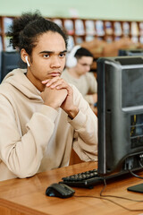 Young Black student wearing wireless earphones sitting in university library looking at computer...