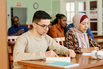 Group of immigrant students in international class sitting at desk reading and making notes during...