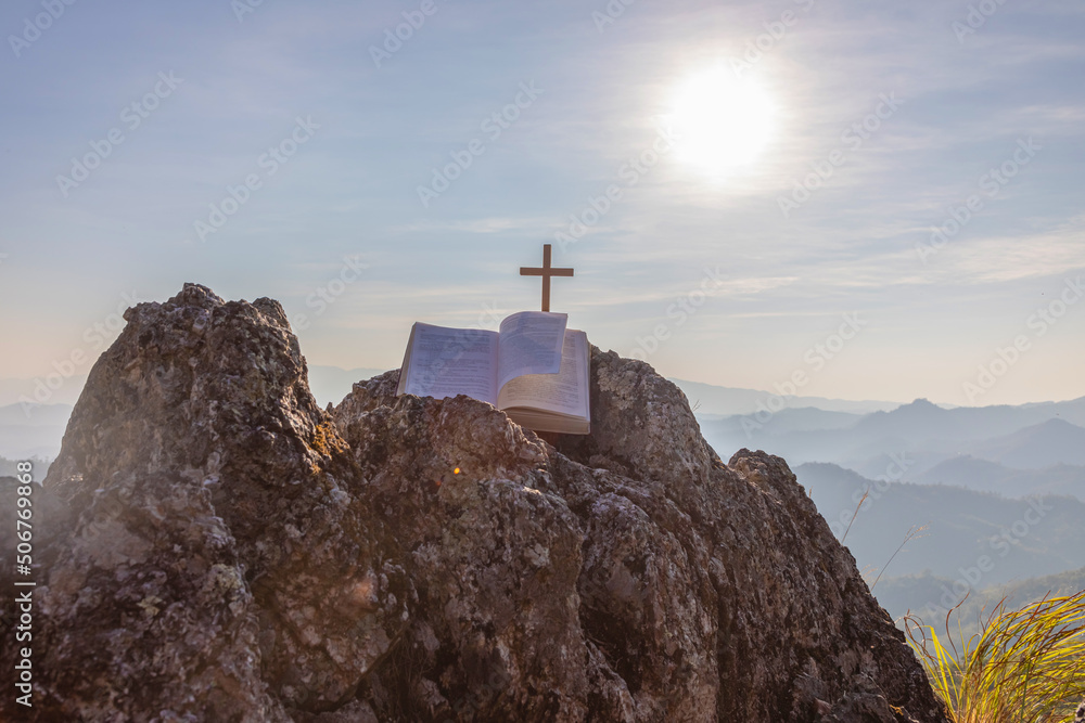 Wall mural crucifix symbol and bible on top mountain with bright sunbeam on the colorful sky background