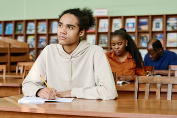 Pensive young Black man sitting at desk in classroom having lesson at international school for...