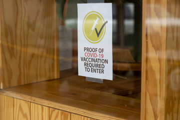 Closeup of a "Proof of Covid-19 Vaccination Required To Enter" sign on a restaurant window.