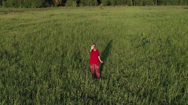 elderly female standing in  meditation pose in  field,  summer meadow with green grass. Drone video flying around person