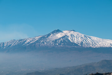 Panoramic view of snow capped Mount Etna volcano on a sunny day seen from Taormina, island Sicily, Italy, Europe, EU. Slopes of black lava stones. Travel destination with mountain landscape, craters