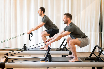 Athletic men doing squats on pilates machine