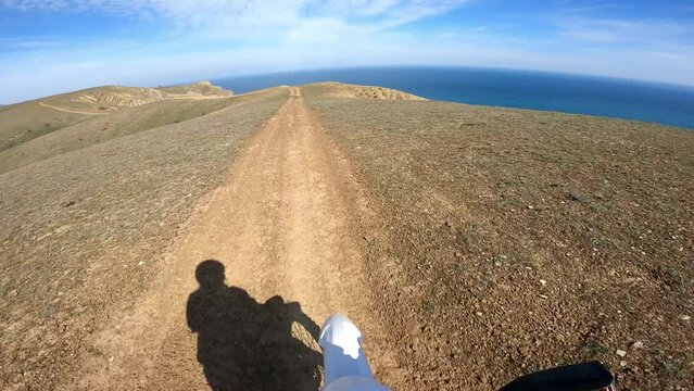 steering wheel driver view of motorcyclist riding off-road motorcycle on mountain ridge overlooking the blue sea