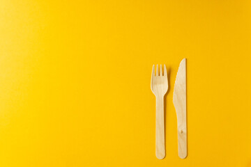 Disposable tableware from natural materials - wooden fork and knife isolated on a yellow background.