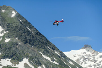 A rescue helicopter flying over the Alpine lake in Austria. Rescue mission. The artificial lake stretches over a vast territory, shining with navy blue color. The dam is surrounded by high mountains