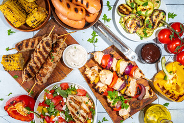 Grilled summer bbq dishes. Bar-b-q party picnic flatlay with various barbecue grill food - shish kebab skewers, grilled corn, salad with bonfire fried chicken, steak, sausages, vegetables top view