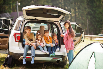 Family of four kids and mother at vehicle interior. Children sitting in trunk. Traveling by car in the mountains, atmosphere concept.
