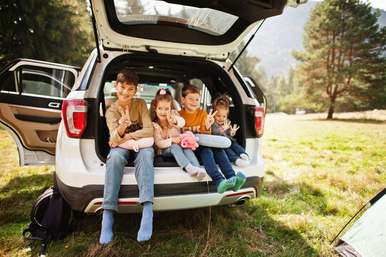 Family of four kids at vehicle interior. Children sitting in trunk. Traveling by car in the mountains, atmosphere concept.