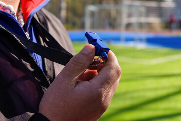 A sport coach with a whistle ready to command the team outdoors, on the football green field
