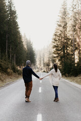 A couple in love is walking on an epmty road in the forest. Holding hand and keeping distance as...