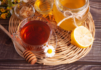 Cup of herbal tea with lemon and honey in jar on the tray.