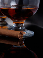A glass of cognac and a cigar on a black background